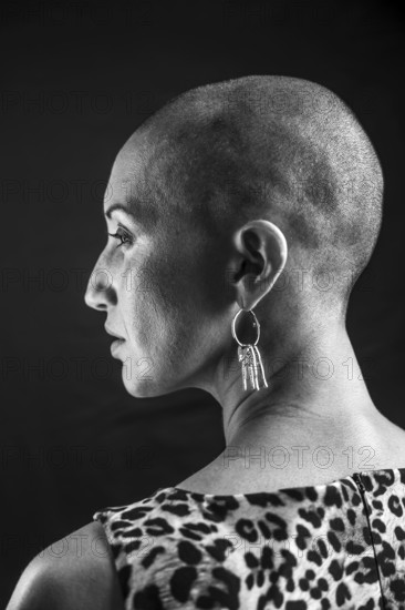 Black and white portrait of a bald woman in profile, showcasing elegant earrings and a patterned