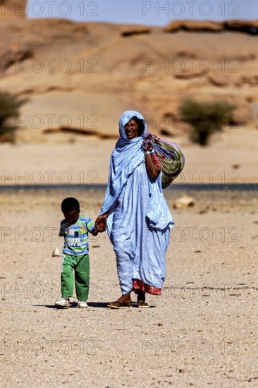 Mother and child, both in traditional dress, walking through a barren desert landscape, woman in