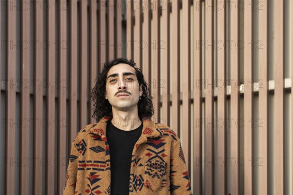 Portrait of a confident man with a mustache, wearing a patterned jacket, standing against a modern