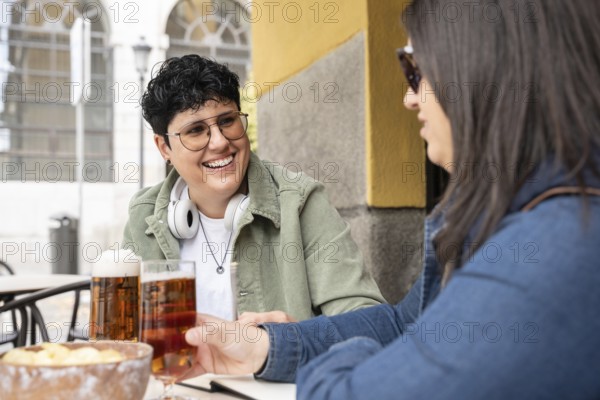A joyful scene of a curvy lesbian couple enjoying beers at a bar. They appear relaxed and happy,