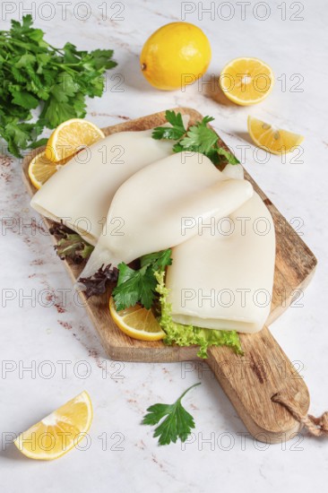 Fresh squid prepared for cooking, surrounded by herbs and lemon, placed on a wooden chopping board