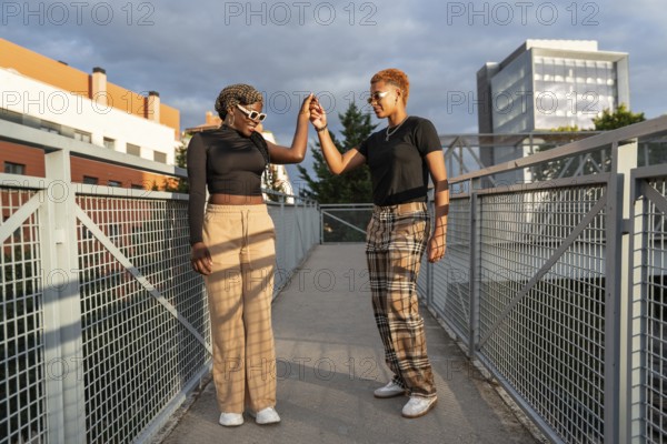 A cheerful LGBT multiethnic couple enjoys a sunny day on an urban bridge, holding hands and