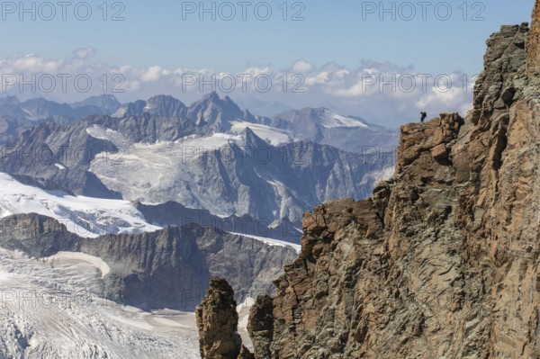 A hiker stands atop a rugged cliff in Zermatt, Switzerland, admiring the panoramic summer view of