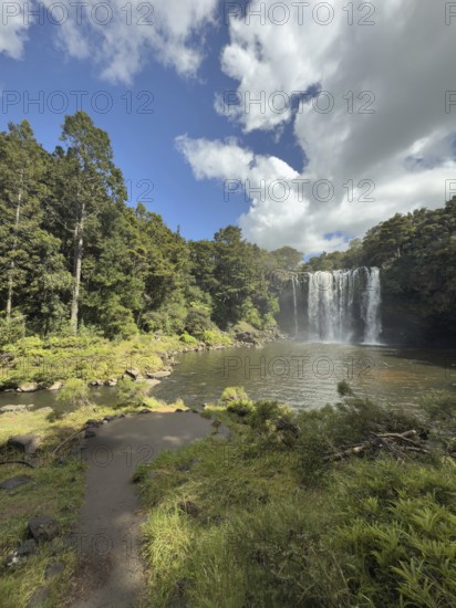 Rainbow Falls waterfall (Waianiwaniwa) amidst lush trees under blue sky with cloudy water,