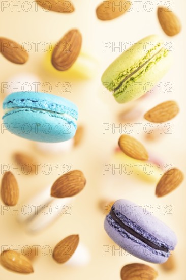 Multicolored flying macaroons and almonds frozen in the air on blurred beige background. top view,