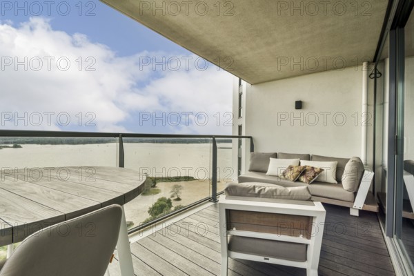 A stylish balcony featuring a cozy seating area overlooking a serene water view and bright sky,