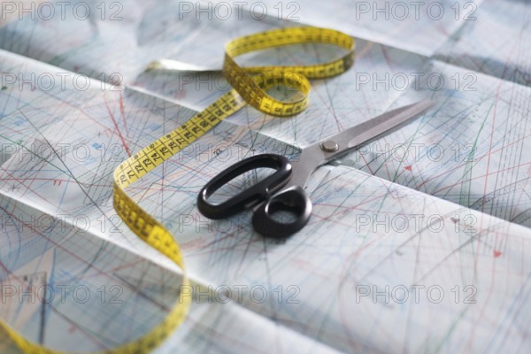 Scissors and a yellow measuring tape rest on detailed sewing pattern paper. This setup captures the