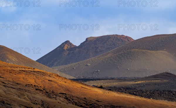 Scenic view of Timanfaya National Park's dramatic volcanic landscape with sunlit hills and rugged