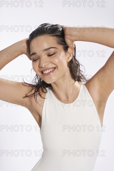 A young female model with wet hair and scattered drops of water on her face is captured smiling