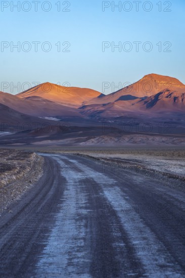 A serene evening view of a winding road meandering through the vibrant hues of orange-lit mountains