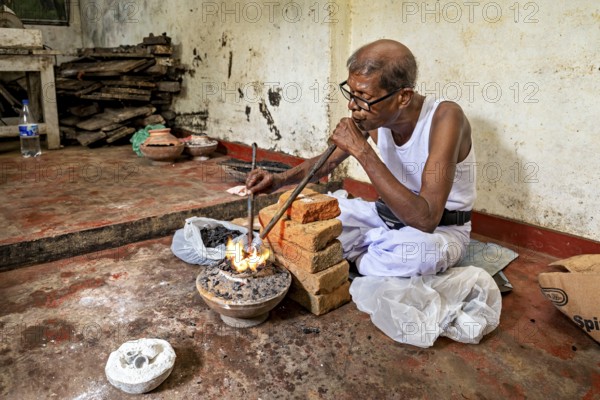 A man blows into a coal-fired pool with a concentrated face, a man burns sapphires in a small stove