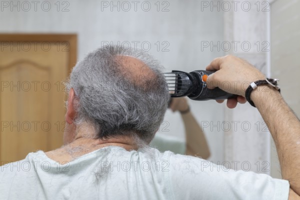 A man cuts his gray hair with electric clippers. The scene captures a home-style haircut in a