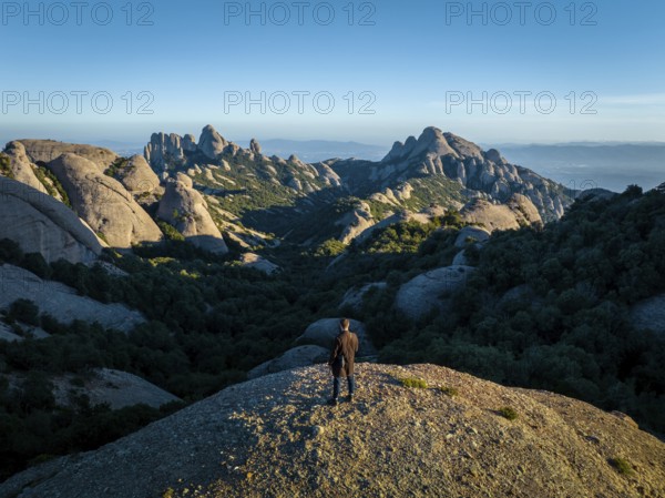 A person stands on a rocky hill, overlooking the stunning Montserrat mountains in Catalonia, Spain,