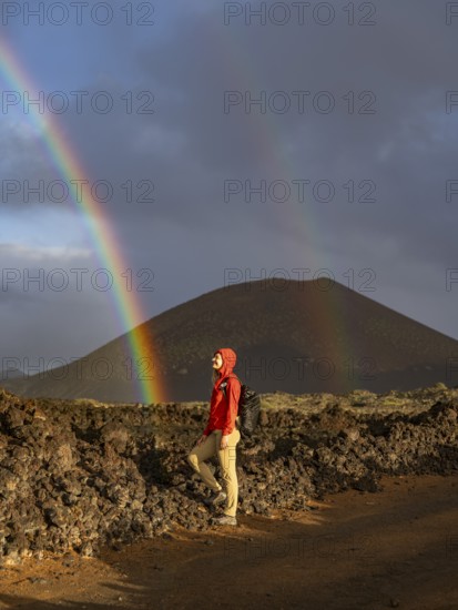 A woman in a red jacket stands on volcanic terrain in Timanfaya National Park, Lanzarote. A vivid