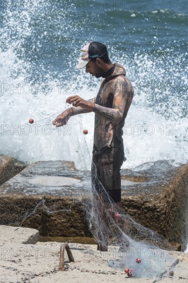 Alexandria, Egypt. June 26th 2024. A young Egyptian fisherman wearing a wetsuit arranges his net on