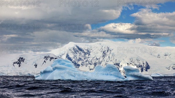 Icebergs floating in undulating water against a backdrop of snow-capped mountains under a dramatic
