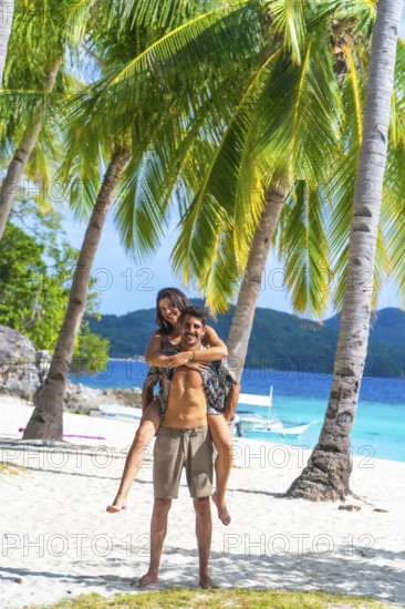Tourists having fun on a beautiful white sand beach with turquoise water and palm trees on