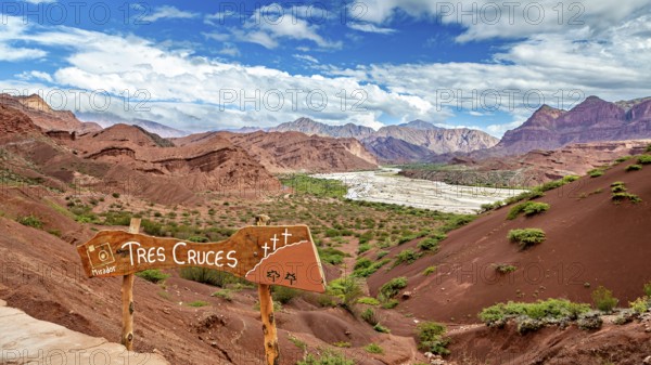 Red mountain landscape with vegetation and a sign in the foreground under a blue sky, The landscape