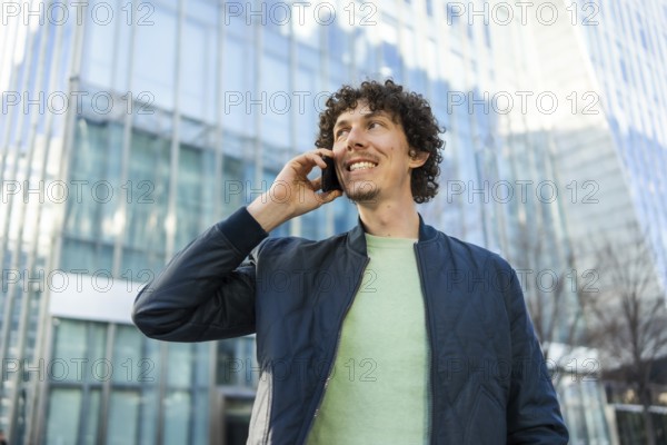 A businessman holds a phone to his ear while walking outside a modern glass building. The image