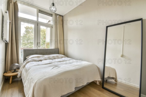 A stylish, serene bedroom featuring a bed with soft bedding, a large mirror, and bright natural
