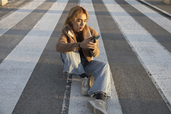 A Mixed-race woman sits quietly at a crosswalk, absorbed in her smartphone Natural light enhances