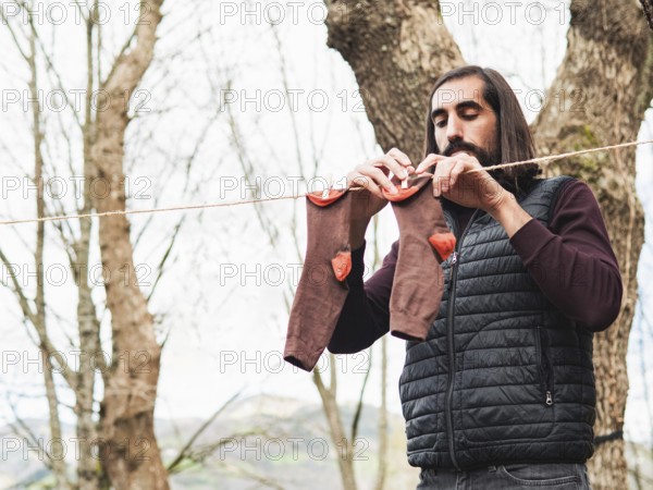 A man hangs clothes on a line in a forest, emphasizing simplicity and nature. The scene highlights