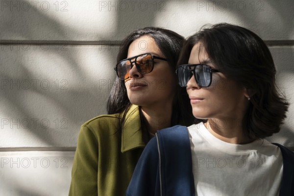 A fashionable lesbian couple wearing stylish sunglasses basks in warm sunlight, casting soft