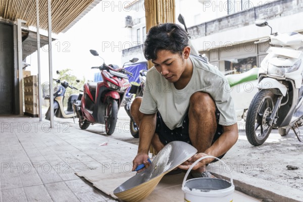 A Balinese artist skillfully paints a sculpture outdoors, blending traditional techniques with