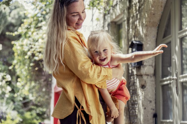 A joyful mother lovingly holds her daughter in an outdoor setting, surrounded by nature. The scene