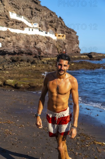 Young hispanic man walking on the beach of tufia, a coastal village of gran canaria, canary