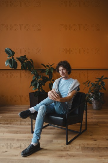 A young man with curly hair sits in a stylish chair in a contemporary room. The space features a