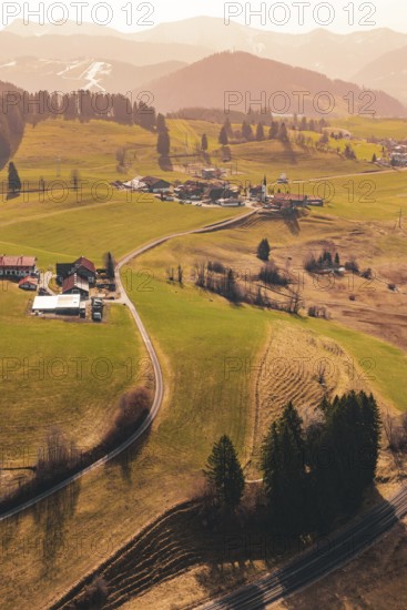 A small village is nestled in rolling hills and green meadows, surrounded by mountains, Oberreute,