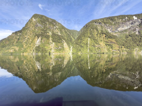 Mountains with reflections in the water against a blue sky in Doubtful Sound, South Island, New