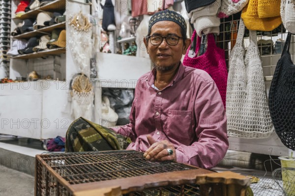 A balinese vendor in a traditional market, wearing glasses. Surrounded by various handmade items