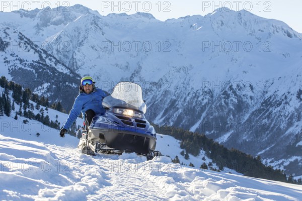 A rider on a snowmobile speeds through a snow-covered mountainous landscape, capturing the thrill