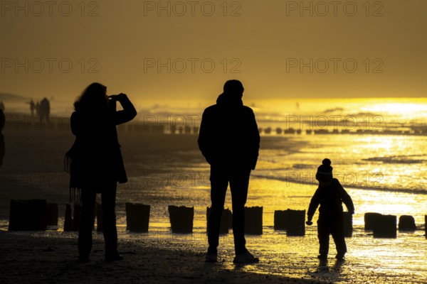 Winter on the North Sea, sunset at sea, beach walkers, coastal protection, through wooden posts,