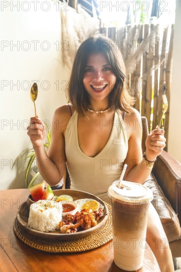 Young woman holding cutlery and smiling, ready to enjoy traditional filipino breakfast with iced