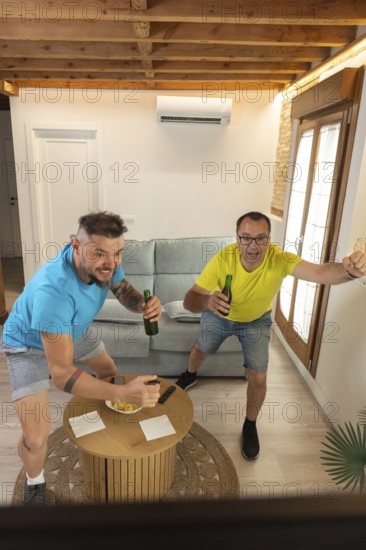 Friends reacting with excitement after a goal while watching a live sports match at home.