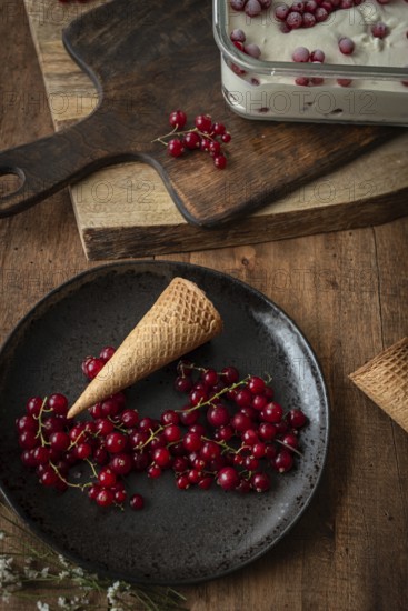 Top view of a rustic food scene featuring red currants on a dark plate beside a waffle cone, set