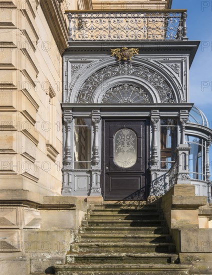 Historic door with filigree decorations and railings on a stone staircase in sunlight, Landau,