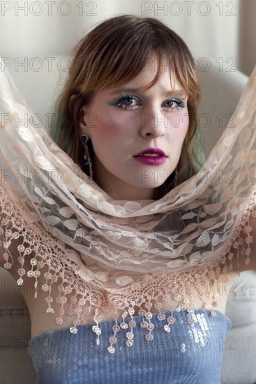 A woman with vibrant makeup and a sequined top poses gracefully, holding a delicate lace shawl Her