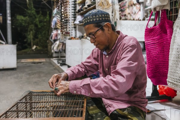 A balinese artisan focuses intently while crafting at a market stall. Surrounded by handmade