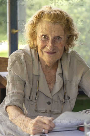 Happy retired woman with curly hair holding a book and smiling, enjoying her leisure time at home,