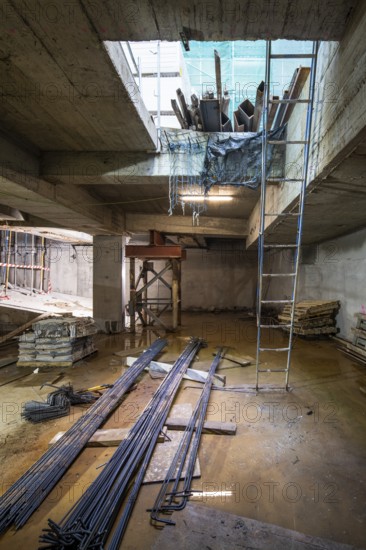 A construction site with steel beams, wooden planks, and a blue ladder. The area is lit naturally,