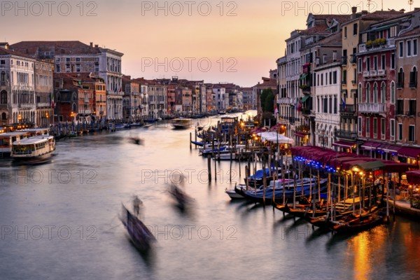 View of the Grand Canal with gondoliers at sunset, picturesque evening mood with illuminated