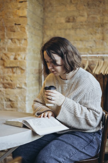 A young woman sits in a charming bookstore, engrossed in a book, while enjoying a hot coffee The