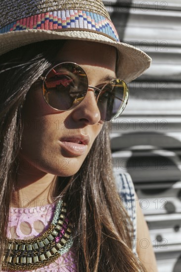 A fashionable woman wearing a straw hat and chic sunglasses. Her long hair and decorative necklace