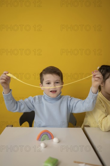 A child joyfully stretches colorful modeling clay during a creative lesson. The bright yellow