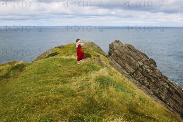 A woman clad in a flowing red dress stands on the rugged cliffs of Middle Cove overlooking the