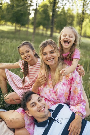 A joyful family shares a happy moment together in a lush green park, laughing and embracing. The